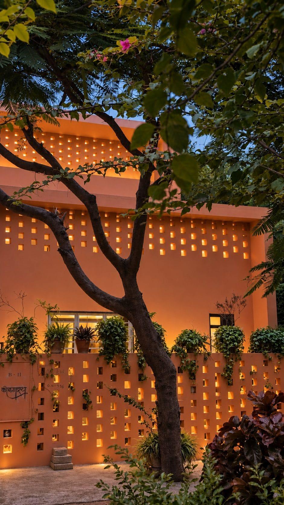 Garden wall and screen lit from within, seen through a tree