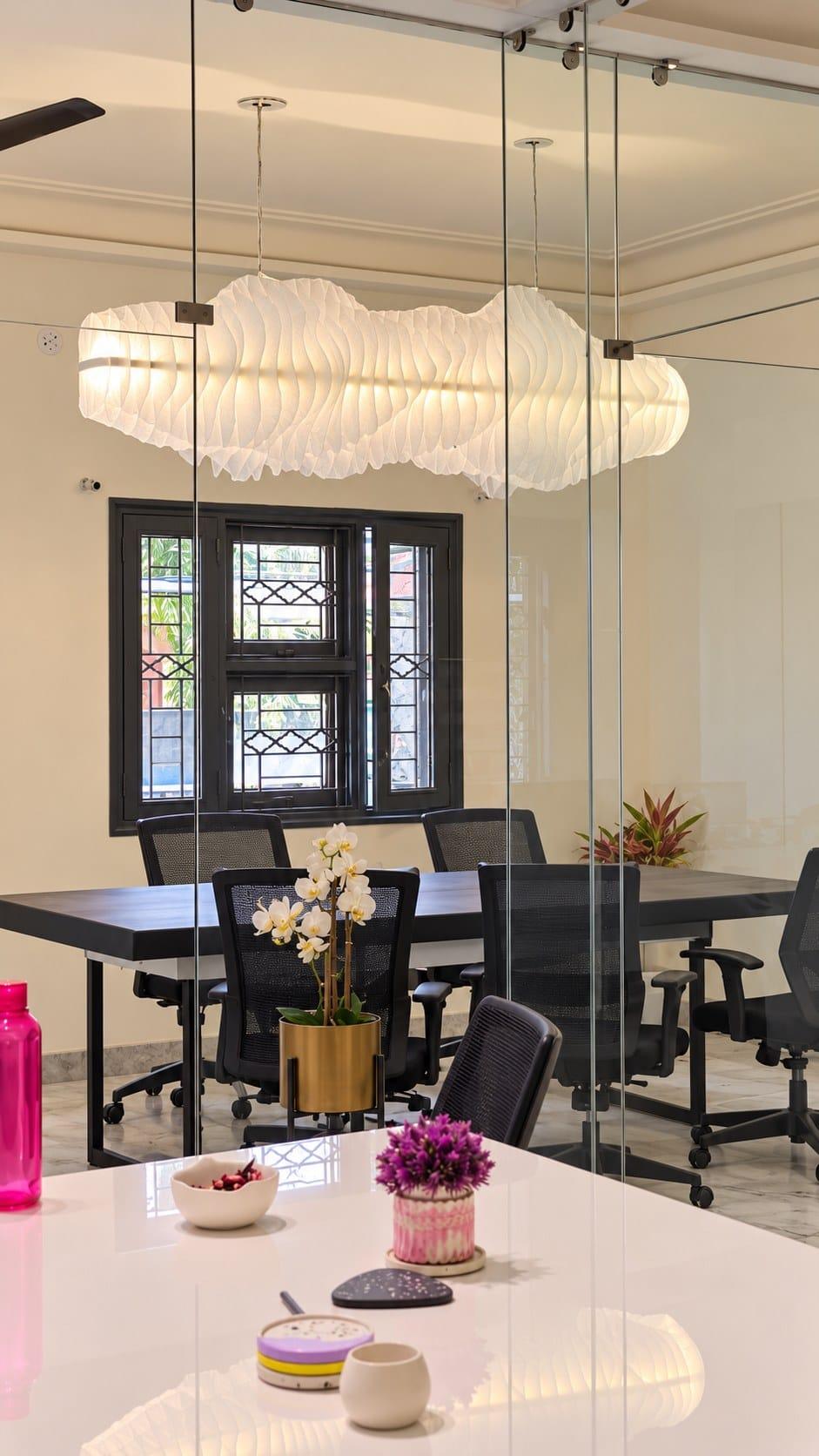 The Indore studio meeting room: a cloud-like paper pendant over a dark table, behind glass, with orchids in the foreground